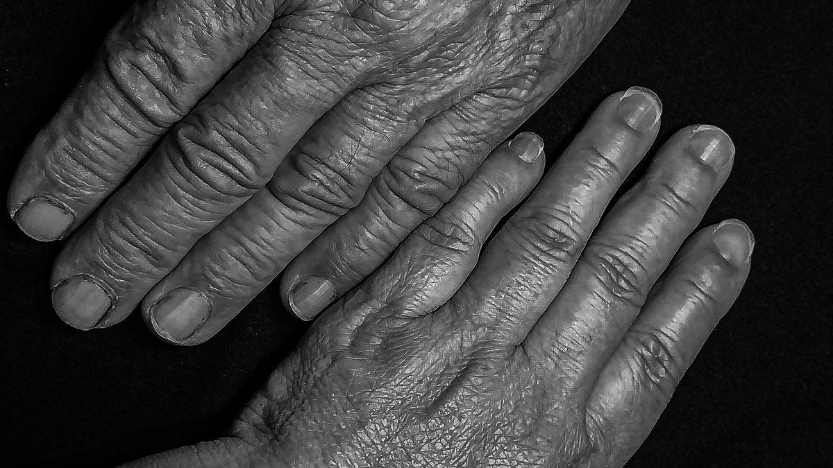 Two pairs of weathered hands resting in soft light.
